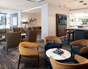 Lobby seating area with contemporary armchairs, marble tables, and warm neutral décor at Courtyard By Marriott Los Angeles LAX/Century Boulevard.