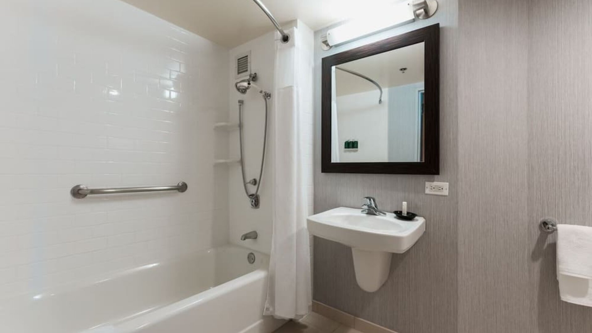 Accessible bathroom with bathtub, grab bars, wall-mounted sink, and modern neutral finishes at Courtyard By Marriott Los Angeles LAX/Century Boulevard.