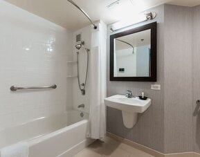 Accessible bathroom with bathtub, grab bars, wall-mounted sink, and modern neutral finishes at Courtyard By Marriott Los Angeles LAX/Century Boulevard.