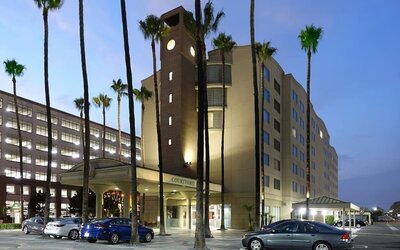 Evening exterior view of the hotel with palm trees, covered entrance, and illuminated façade at Courtyard By Marriott Los Angeles LAX/Century Boulevard.