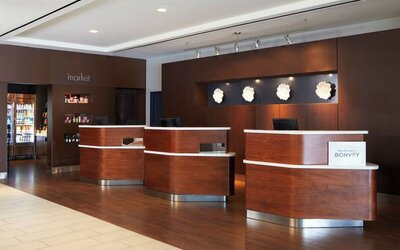 eception desk area with wood finishes, Marriott Bonvoy branding, and adjacent market/snack section at Courtyard By Marriott Los Angeles LAX/Century Boulevard.