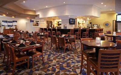 Spacious dining area with restaurant seating, patterned carpet, and central bar area at Embassy Suites By Hilton LAX Airport North.