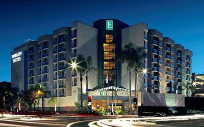Evening exterior view of the hotel building with lit windows and palm-lined street at Embassy Suites By Hilton LAX Airport North.