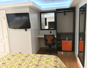 In-room workspace with desk, chair, mini fridge, wall-mounted TV, and open closet area at Mid City Inn - Los Angeles.