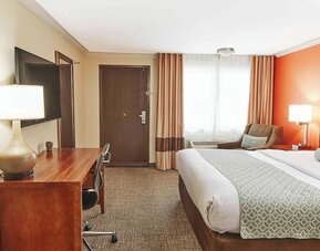 Guest room with king bed, work desk, upholstered chair, and large curtained window at The Hills Inn Eagle Rock.
