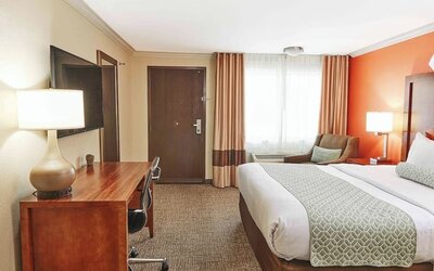 Guest room with king bed, work desk, upholstered chair, and large curtained window at The Hills Inn Eagle Rock.