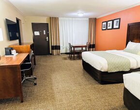 Spacious guest room with two beds, work desk, dining table, and orange accent wall at The Hills Inn Eagle Rock.