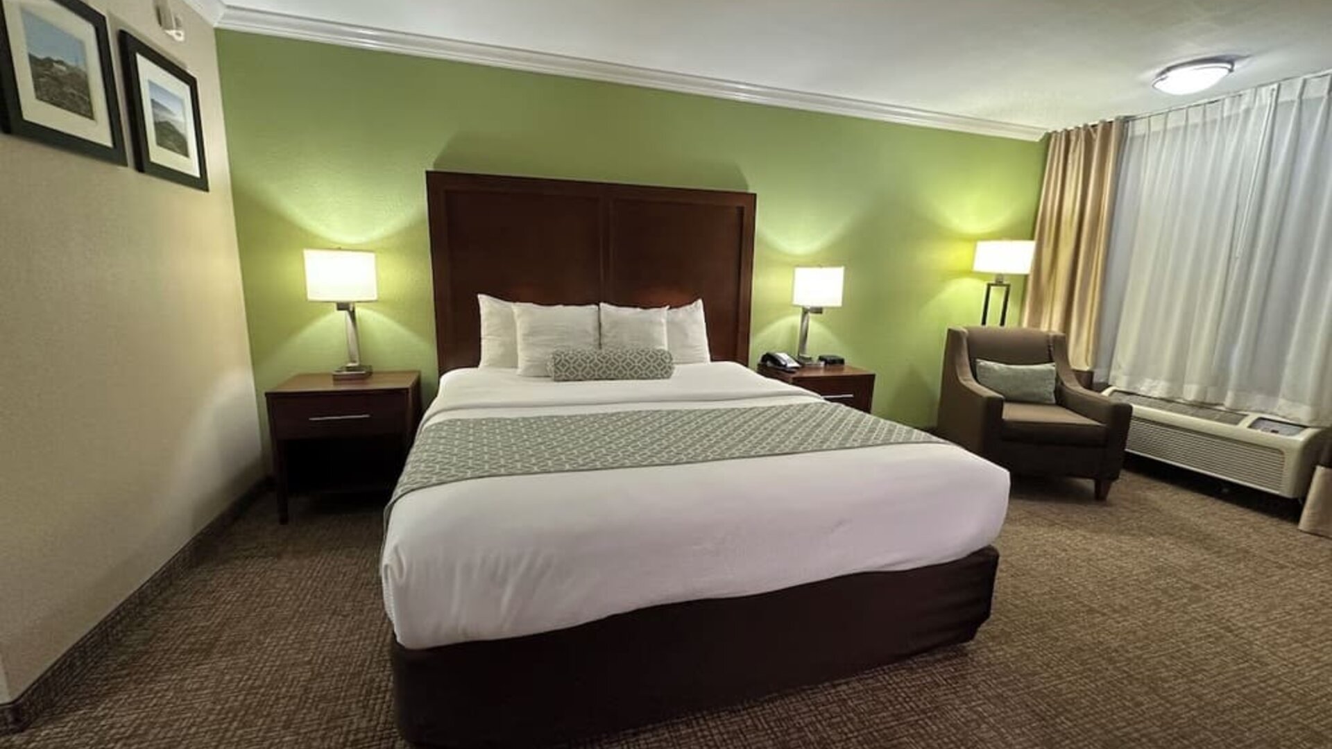 King bedroom with green accent wall, bedside lamps, armchair, and carpeted floors at The Hills Inn Eagle Rock.
