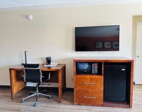 Work area with desk chair, flat-screen TV, microwave, mini fridge, and wood flooring at The Hills Inn Eagle Rock.