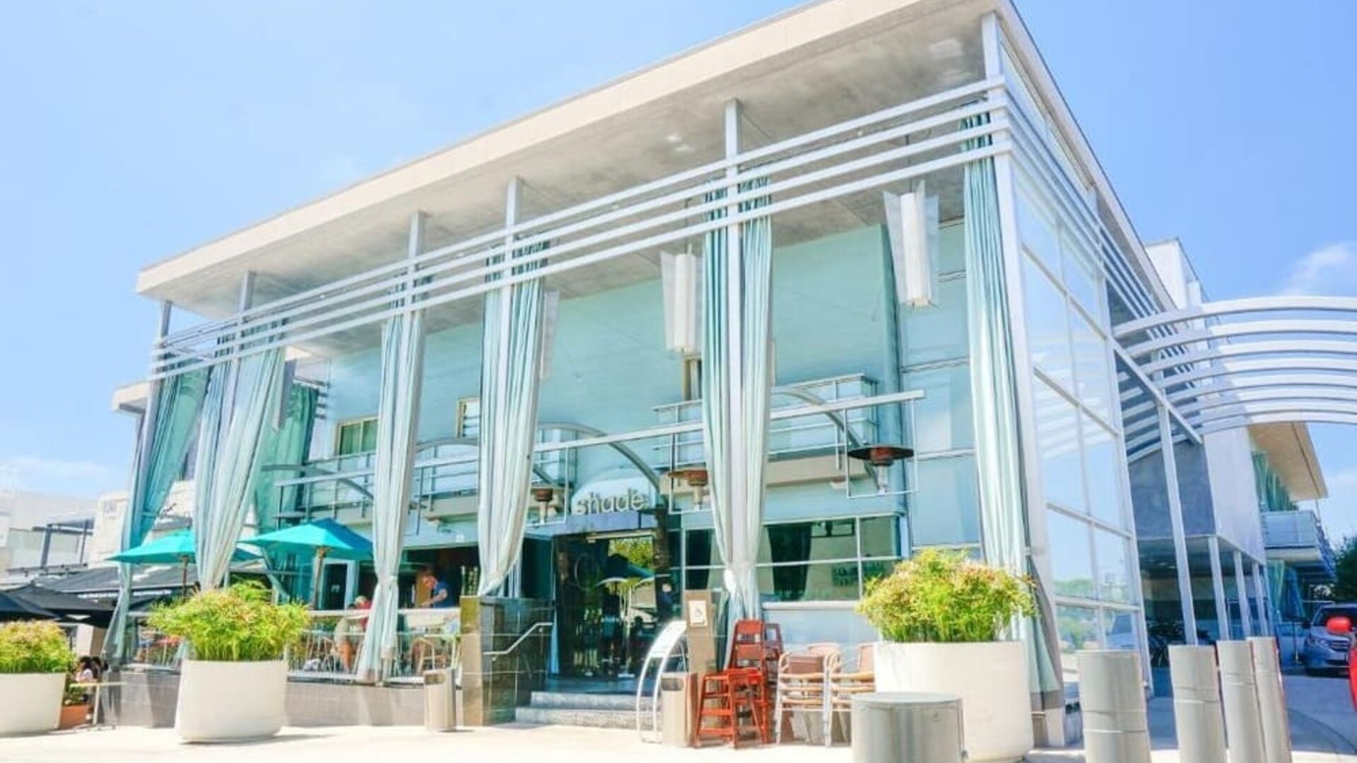 Modern glass-front hotel entrance with tall draped curtains and outdoor seating at Shade Hotel Manhattan Beach.