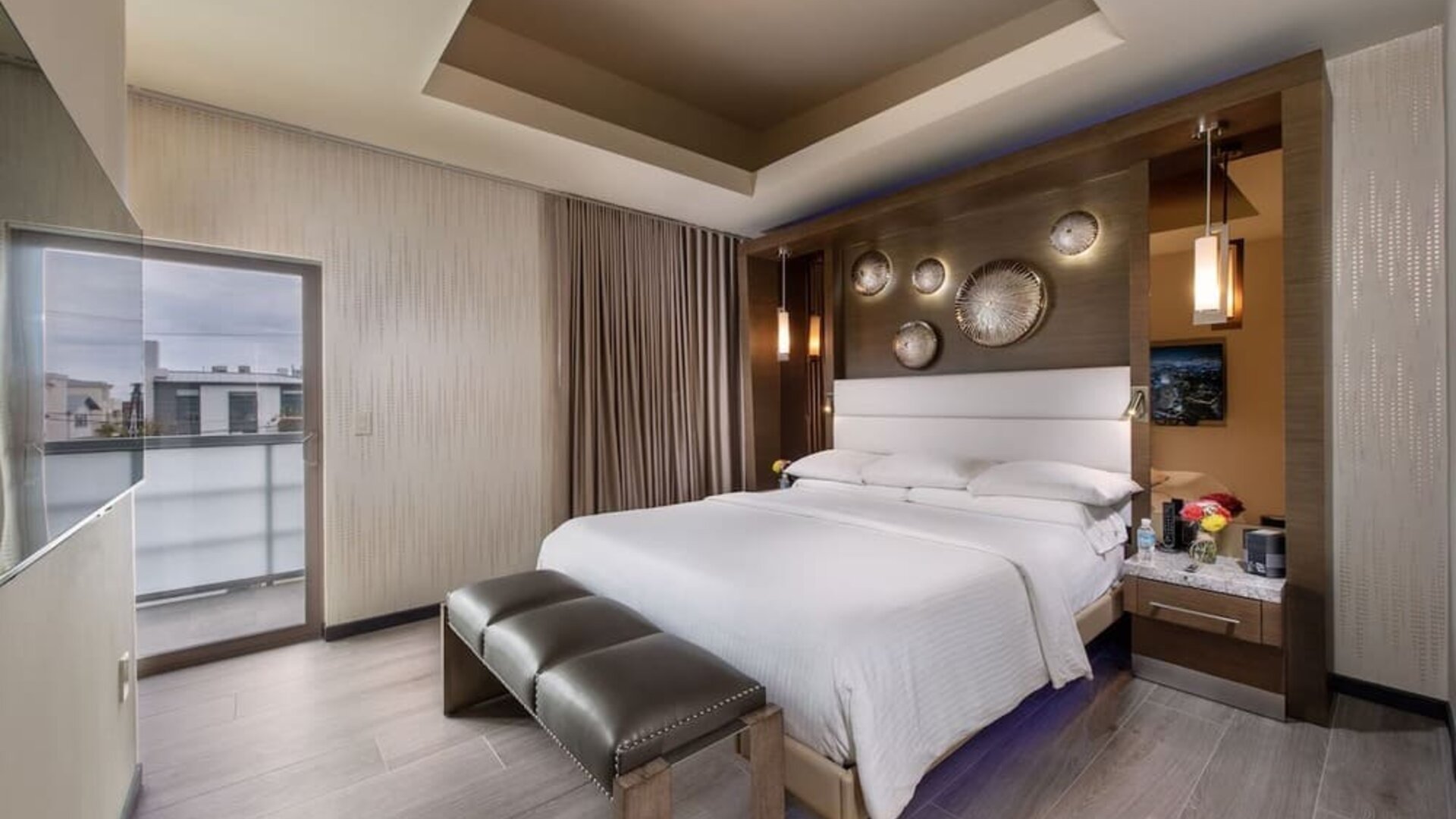 King bedroom with modern decor, padded bench, balcony access, and decorative wall accents at Shade Hotel Manhattan Beach.