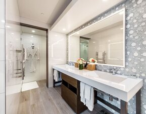 Modern bathroom with double vanity, illuminated mirror, walk-in shower, and patterned wall tiles at Shade Hotel Manhattan Beach.