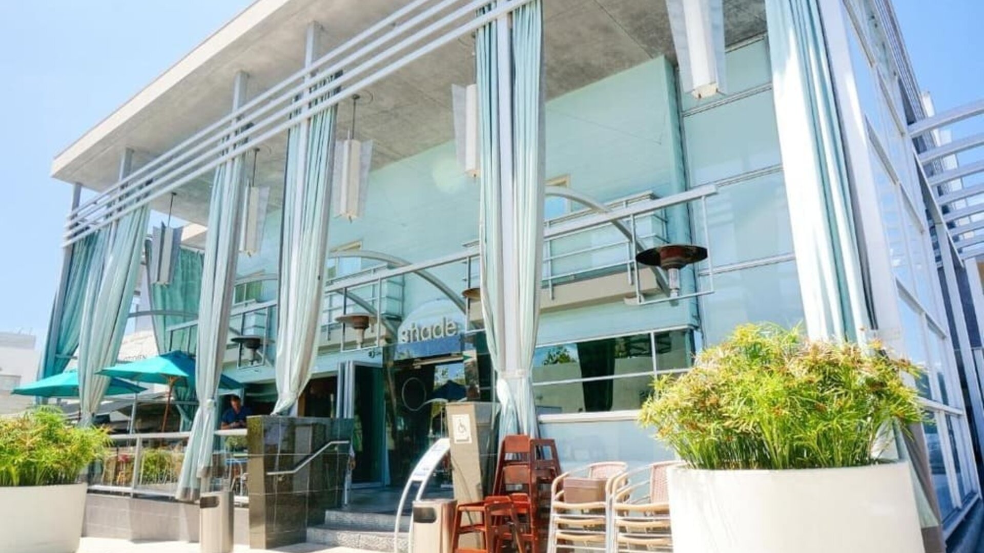 Hotel entrance with floor-to-ceiling windows, outdoor seating, and decorative white drapes at Shade Hotel Manhattan Beach.