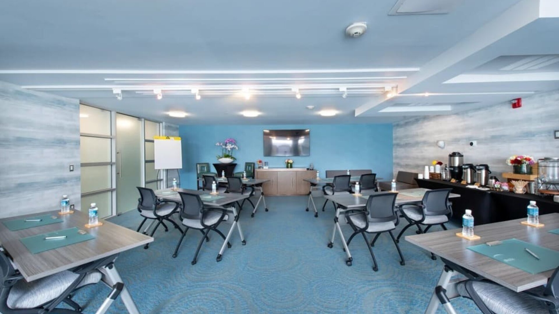 Meeting room with grouped tables, office chairs, presentation screen, and refreshment station at Shade Hotel Manhattan Beach.