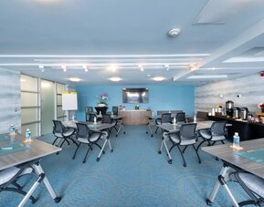 Meeting room with grouped tables, office chairs, presentation screen, and refreshment station at Shade Hotel Manhattan Beach.