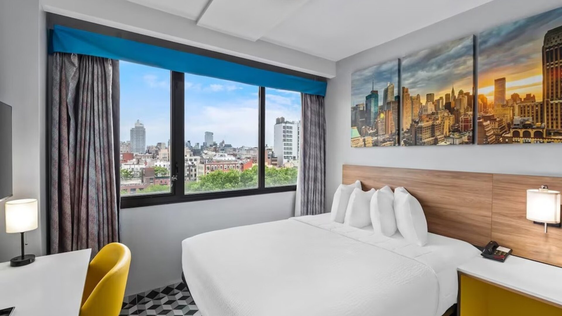 Spacious guest room with large bed, skyline artwork, yellow chair, and expansive city views at Days Inn Chinatown NYC.