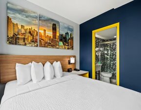 Queen bedroom with bold blue accent wall, skyline artwork, and patterned bathroom tiles at Days Inn Chinatown NYC.