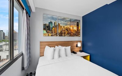 Bright guest room with queen bed, skyline canvas art, and corner city-view windows at Days Inn Chinatown NYC.