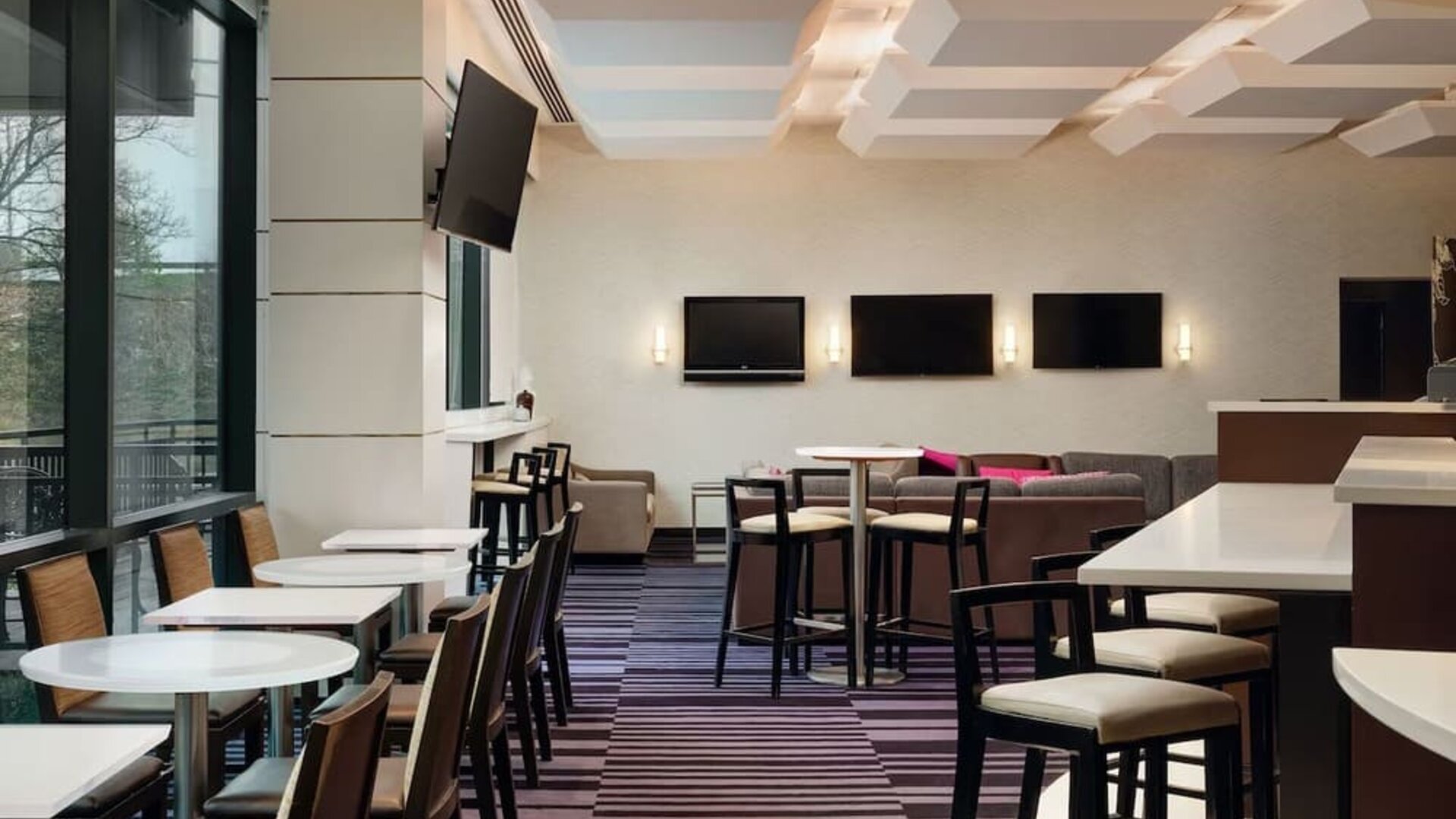 Contemporary dining and lounge area with seating and entertainment screens at Courtyard By Marriott New York JFK Airport.