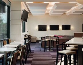 Contemporary dining and lounge area with seating and entertainment screens at Courtyard By Marriott New York JFK Airport.