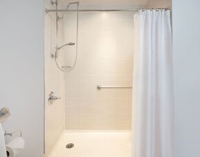 Accessible walk-in shower bathroom with safety handrails at Courtyard By Marriott New York JFK Airport.