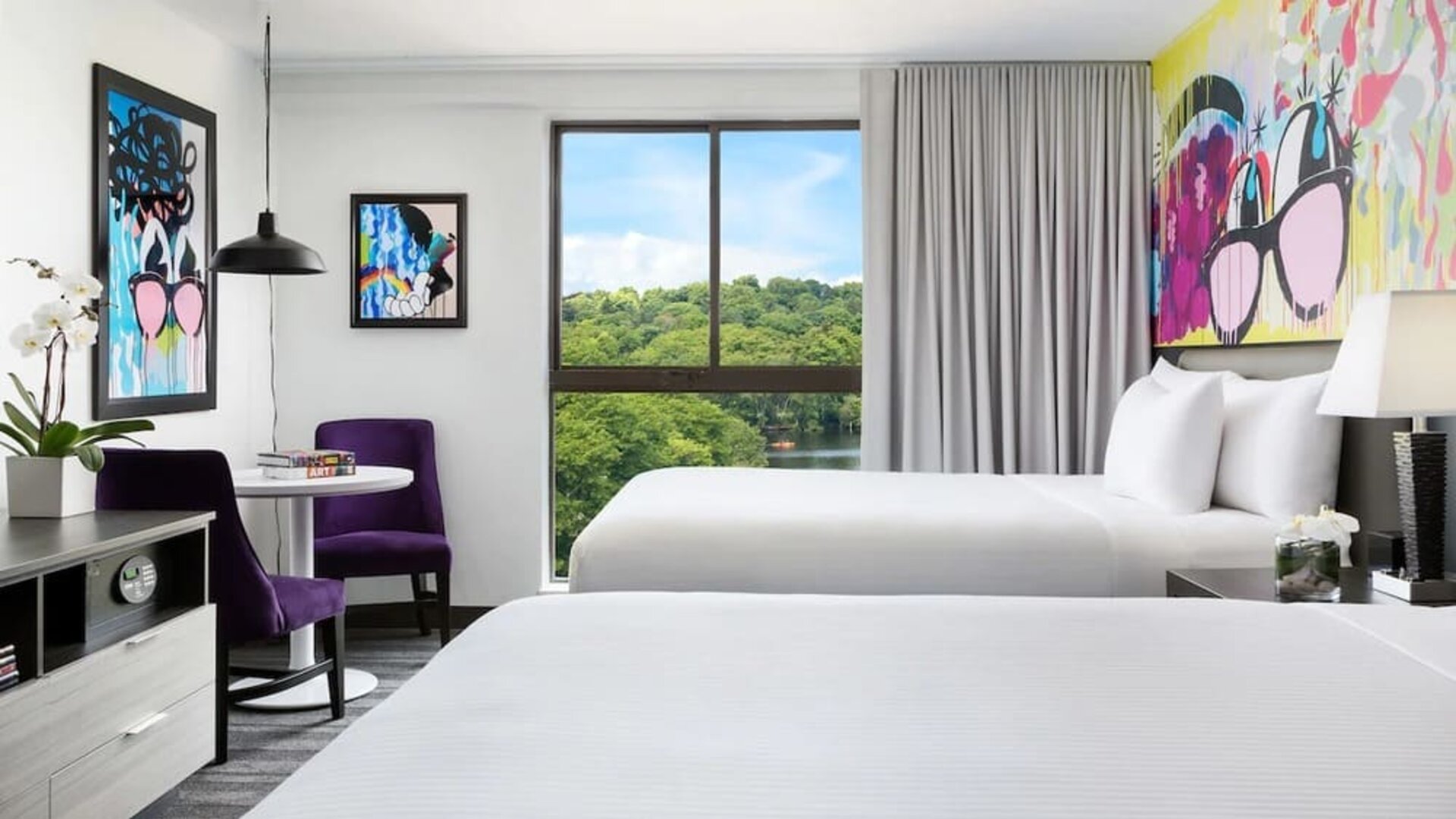 Bright double queen guest room with colorful wall art and large windows at Hotel Studio Allston.
