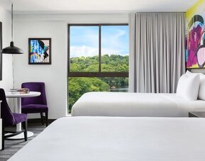Bright double queen guest room with colorful wall art and large windows at Hotel Studio Allston.