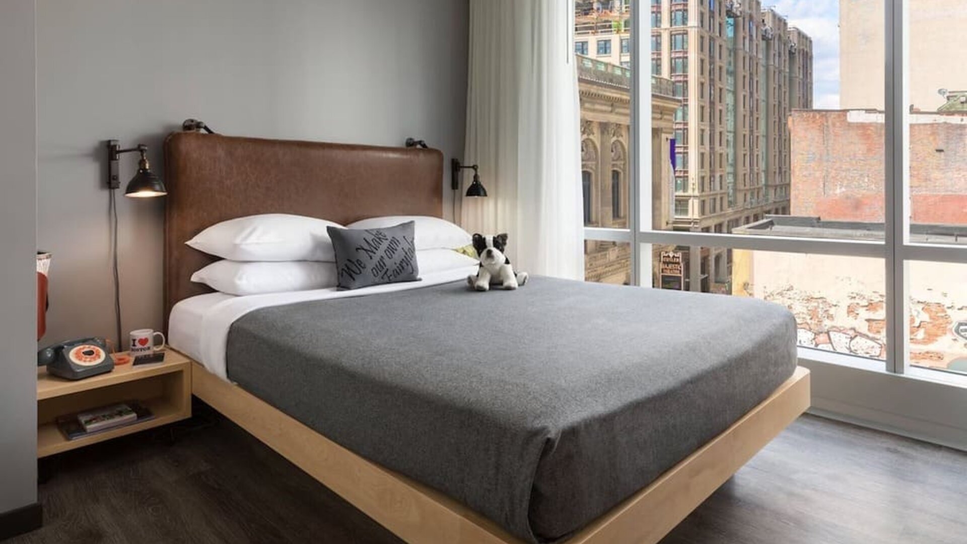 Guest room with leather headboard and large corner windows overlooking downtown Boston at Moxy Boston Downtown.