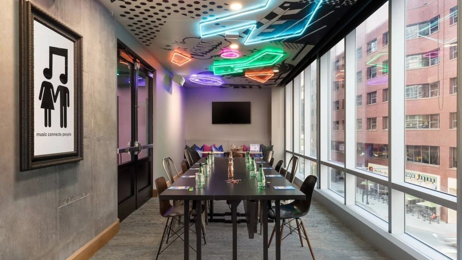 Meeting room with long conference table, neon ceiling accents, and large windows at Moxy Boston Downtown.