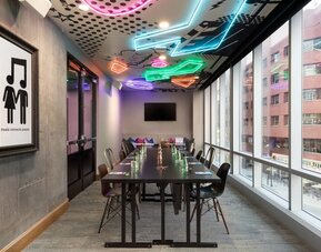 Meeting room with long conference table, neon ceiling accents, and large windows at Moxy Boston Downtown.