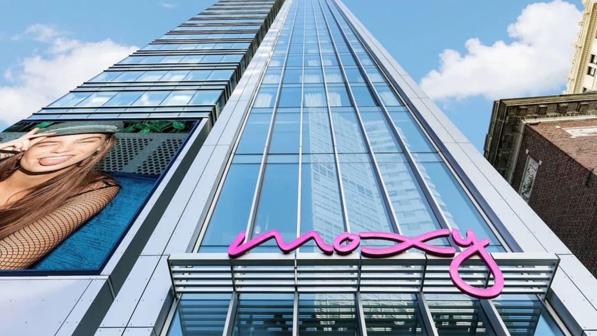 Glass high-rise hotel exterior with bright pink Moxy signage at Moxy Boston Downtown.