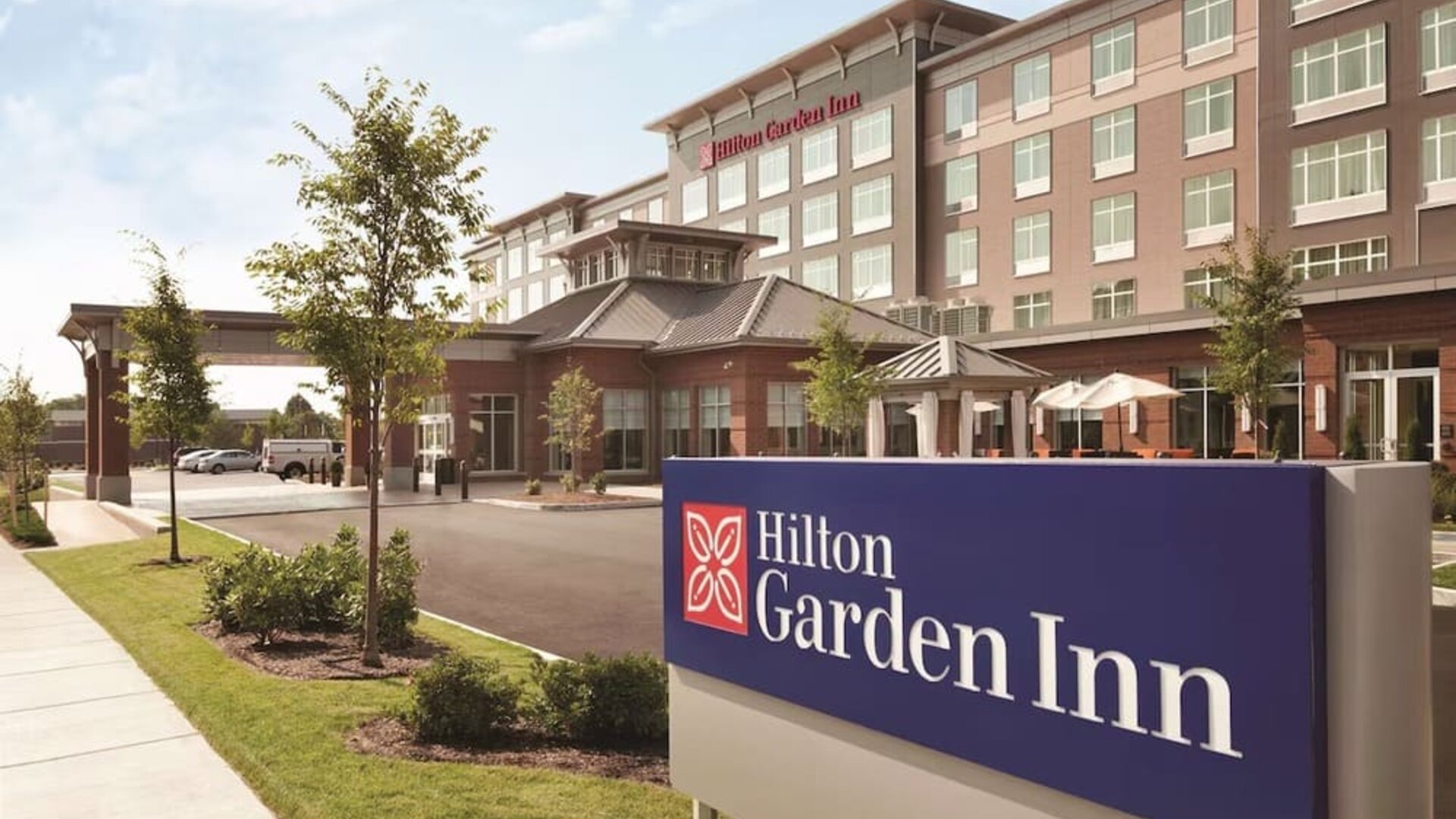 Daytime exterior of Hilton Garden Inn Boston Logan Airport with branded roadside signage and landscaped entrance.