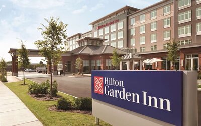 Daytime exterior of Hilton Garden Inn Boston Logan Airport with branded roadside signage and landscaped entrance.
