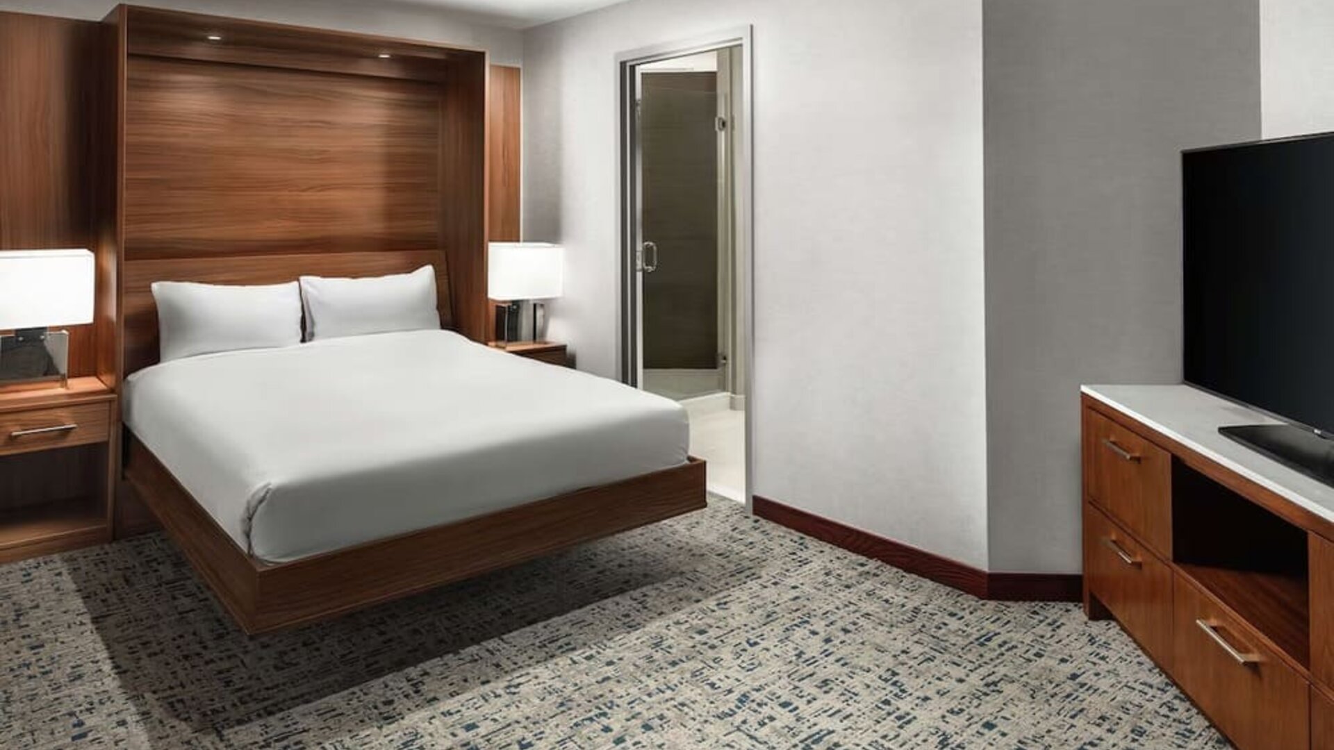 Guest room with platform bed, wood headboard, carpeted floor, and large TV at Hilton Boston Logan Airport.