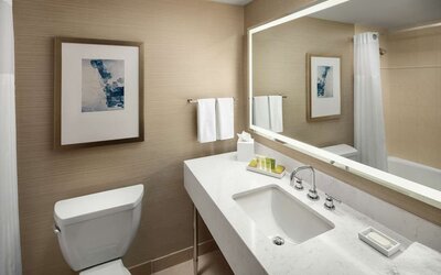 Modern bathroom with illuminated mirror, white vanity countertop, and bathtub shower combo at Hilton Boston Logan Airport.