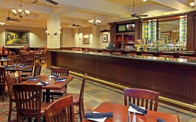 Restaurant and bar area with wooden tables, upholstered seating, and stained glass accents at Hilton Boston Logan Airport.