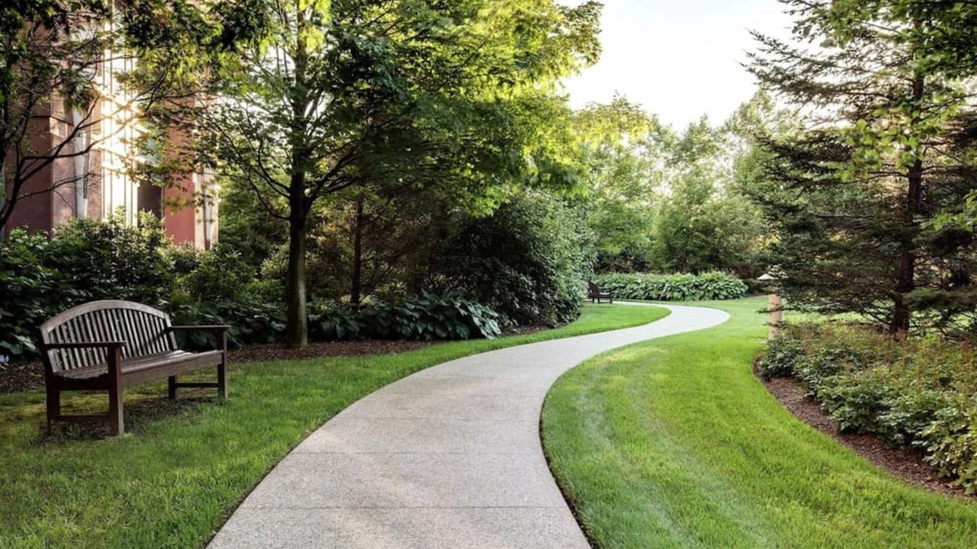 Curved garden walkway with benches, trees, and landscaped greenery at Hilton Boston Logan Airport.