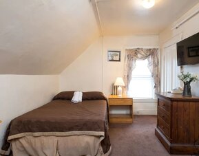 Small attic-style guest room with double bed, wooden dresser, and wall-mounted TV at The Farrington Inn.