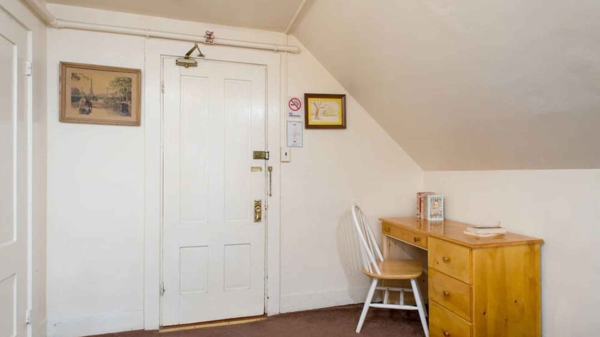 Compact workspace with wooden desk, chair, and sloped ceiling beside entry door at The Farrington Inn.