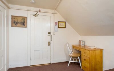 Compact workspace with wooden desk, chair, and sloped ceiling beside entry door at The Farrington Inn.