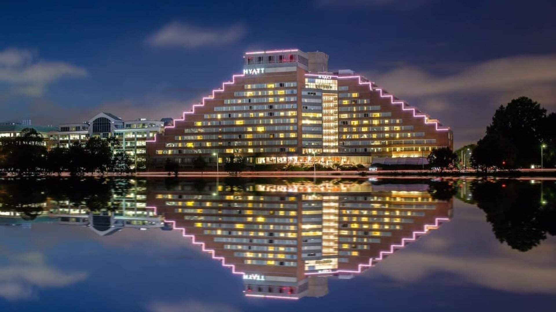 Exterior nighttime view of Hyatt Regency Boston/Cambridge with illuminated pyramid-style architecture reflected on the riverfront.