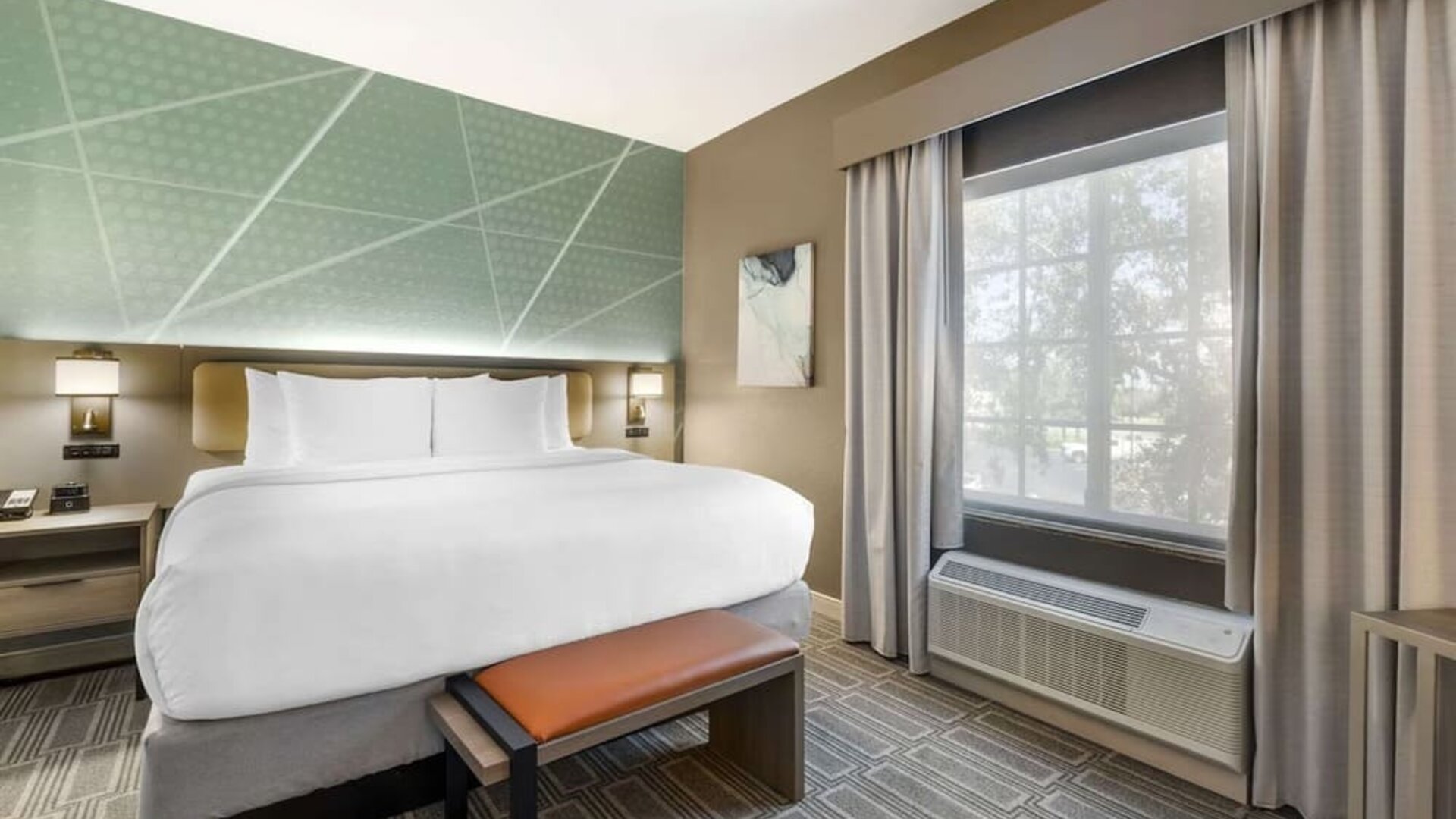 Contemporary king guest room with geometric accent wall, bench seating, and natural light at Comfort Inn & Suites Port Charlotte-Punta Gorda.