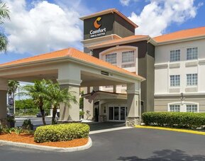 Exterior daytime view of Comfort Inn & Suites Port Charlotte-Punta Gorda with tropical landscaping and covered driveway entrance.