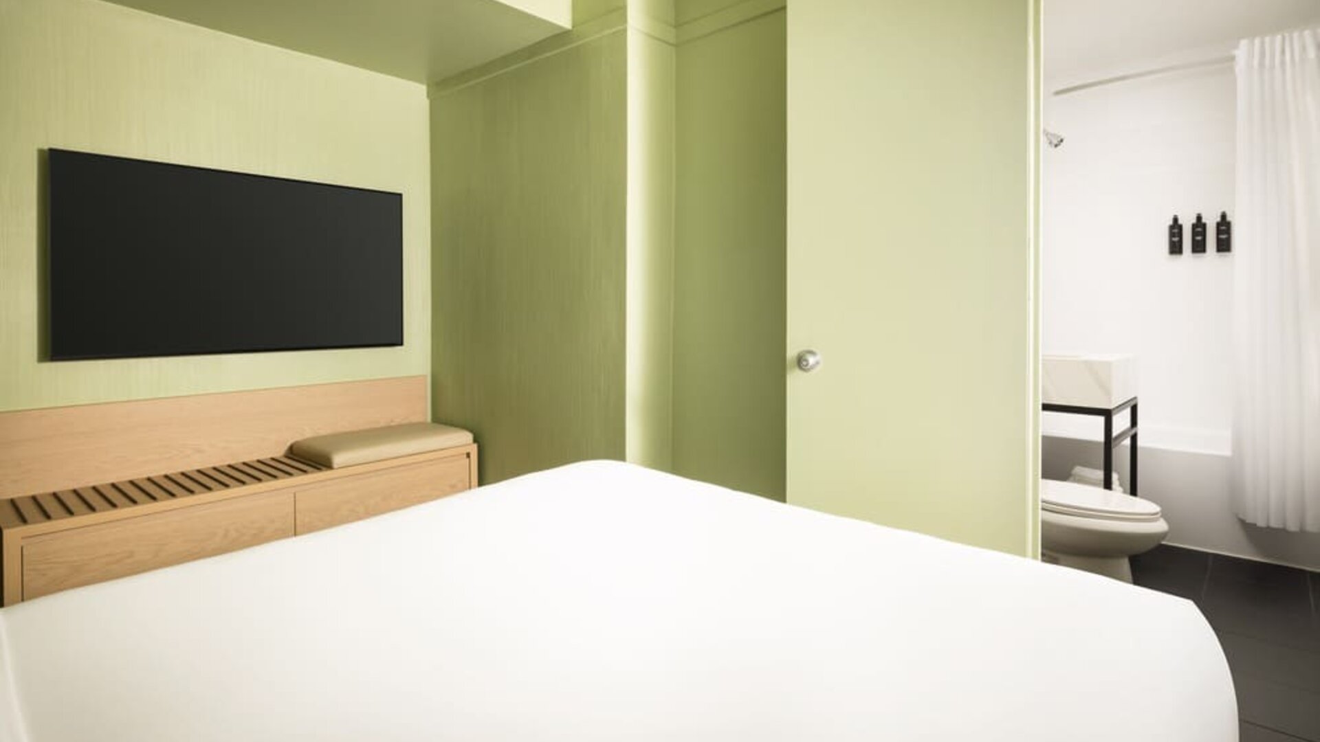 Modern standard guest room with minimalist décor, wall-mounted television, and sleek bathroom access at Row NYC.