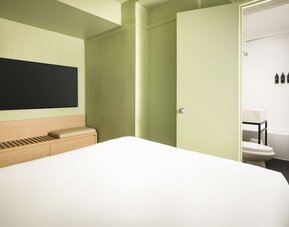 Modern standard guest room with minimalist décor, wall-mounted television, and sleek bathroom access at Row NYC.