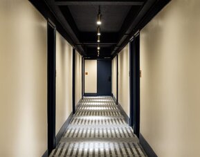 Stylish hotel hallway with patterned carpeting, ambient lighting, and modern guest room entrances at Row NYC.