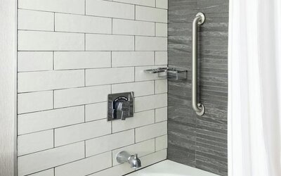 Stylish bathroom with tiled bathtub and rainfall shower fixture featuring sleek modern design at Boston Marriott Newton.