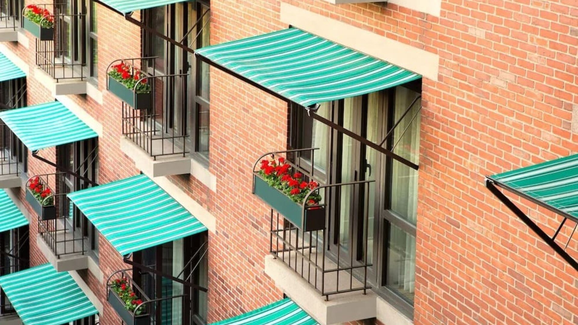 Exterior detail of The Bostonian Boston, A Millennium Hotel featuring charming balconies with striped awnings and flower boxes overlooking the city.