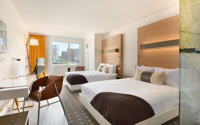 Bright double guest room with two beds, modern furnishings, and large windows offering city views at The Envoy Hotel, Autograph Collection.