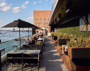 Rooftop outdoor dining terrace overlooking Boston Harbor with lounge seating and scenic waterfront views at The Envoy Hotel, Autograph Collection.